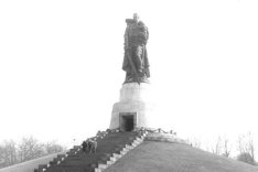 Das Ehrenmal ist von unten fotografiert, die Statue des Soldaten auf einem Sockel am Ende einer Treppe ist im oberen Bildviertel. Groß im Vordergrund ist die weiße Zierpflasterung am Boden.