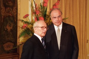 Honecker steht links neben Kohl. Im Hintergrund ein golden gerahmtes Bild und ein großer Blumenstrauß.