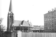 Der Blick geht in den Grenzstreifen. Die Mauer besteht hier teilweise noch aus Fassadenresten abgerissener Grenzhäuser. Im Vordergrund sind Y-förmige Stacheldrahthalter auf der Mauerkrone.